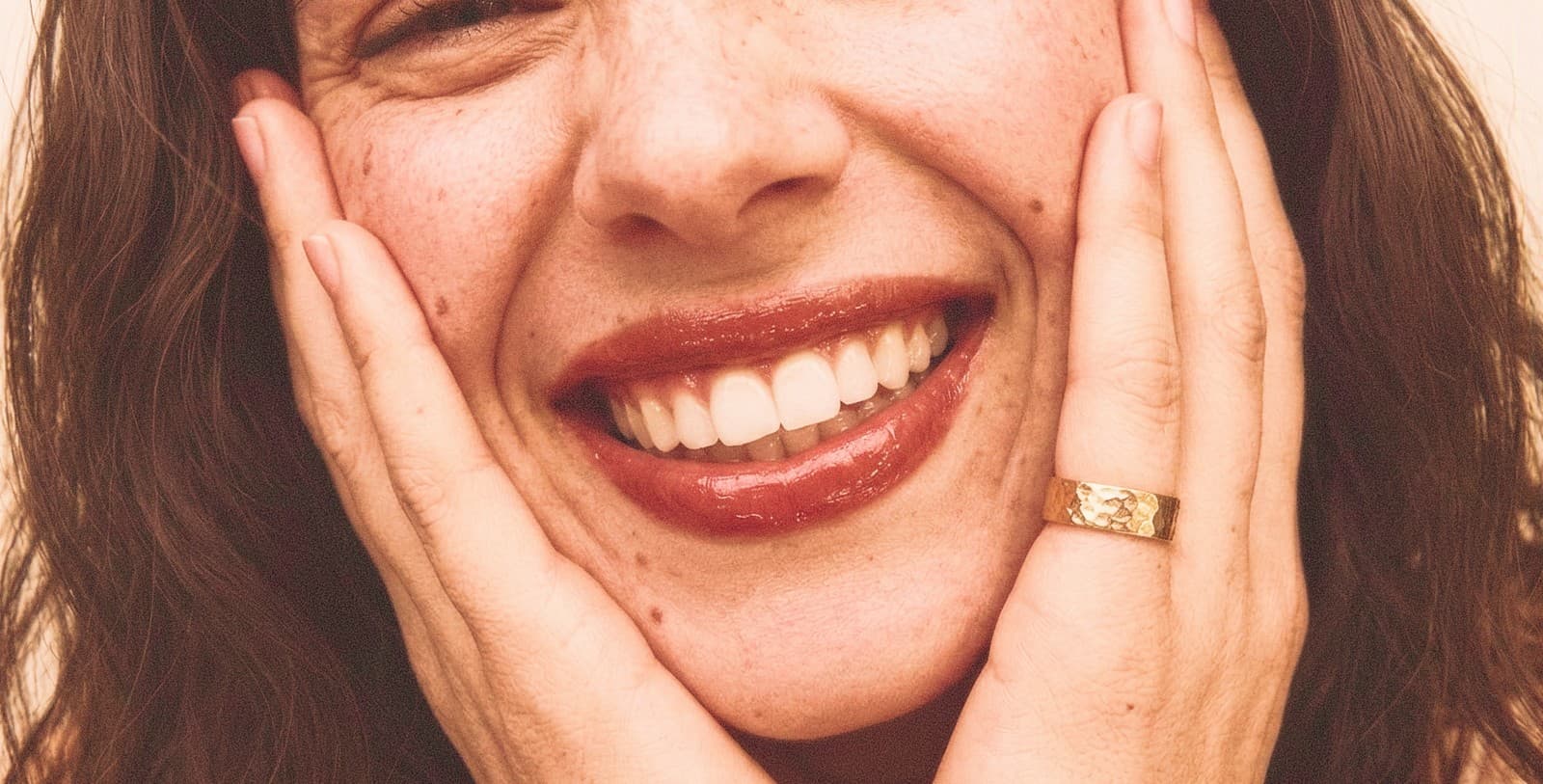 A close-up of someone smiling, chin resting on their hands